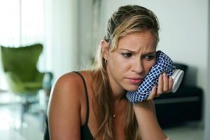 Женщина держит лед на щеке Девушка держит лед на щеке